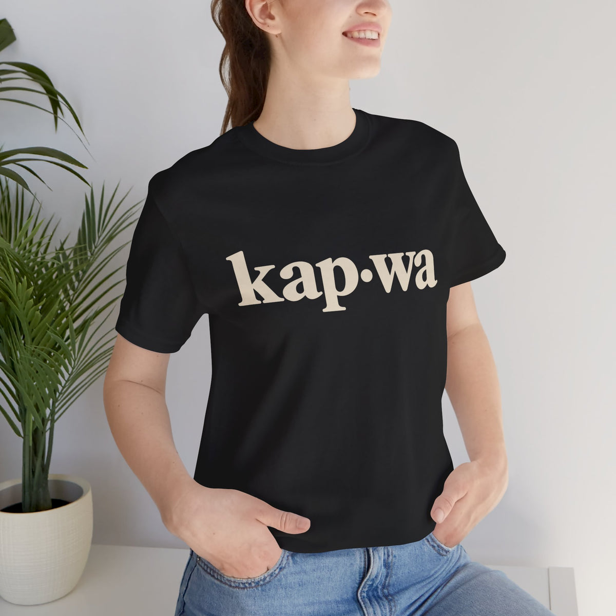 Seated model wearing the Black KAPWA Filipino heritage tee, styled casually with the front graphic visible.