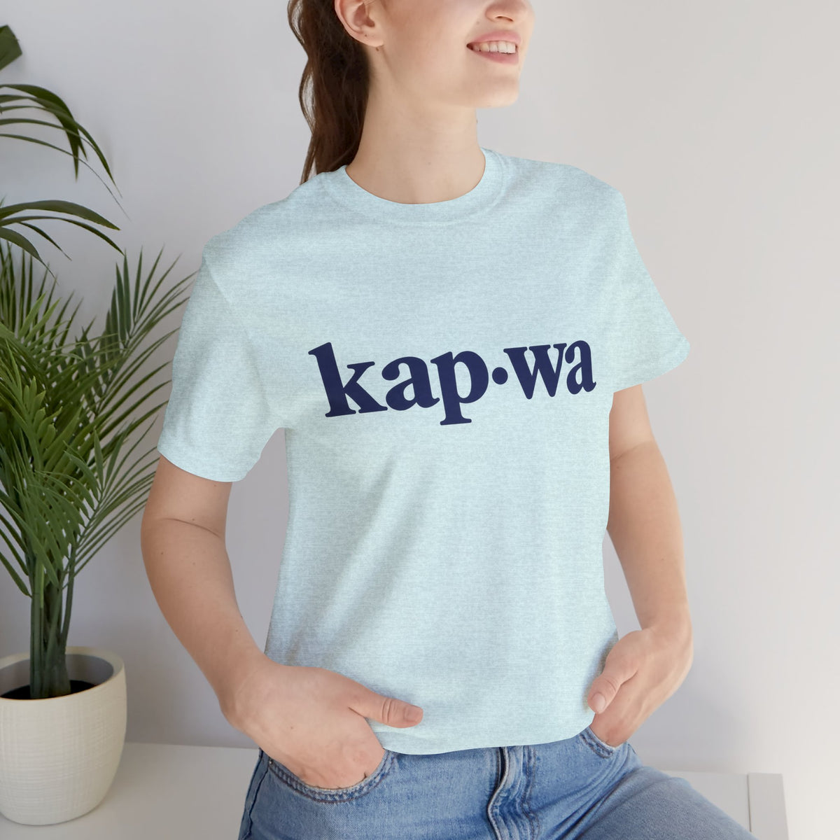 Seated model wearing the Heather Prism Ice Blue KAPWA Filipino heritage tee, styled casually with the front graphic visible.