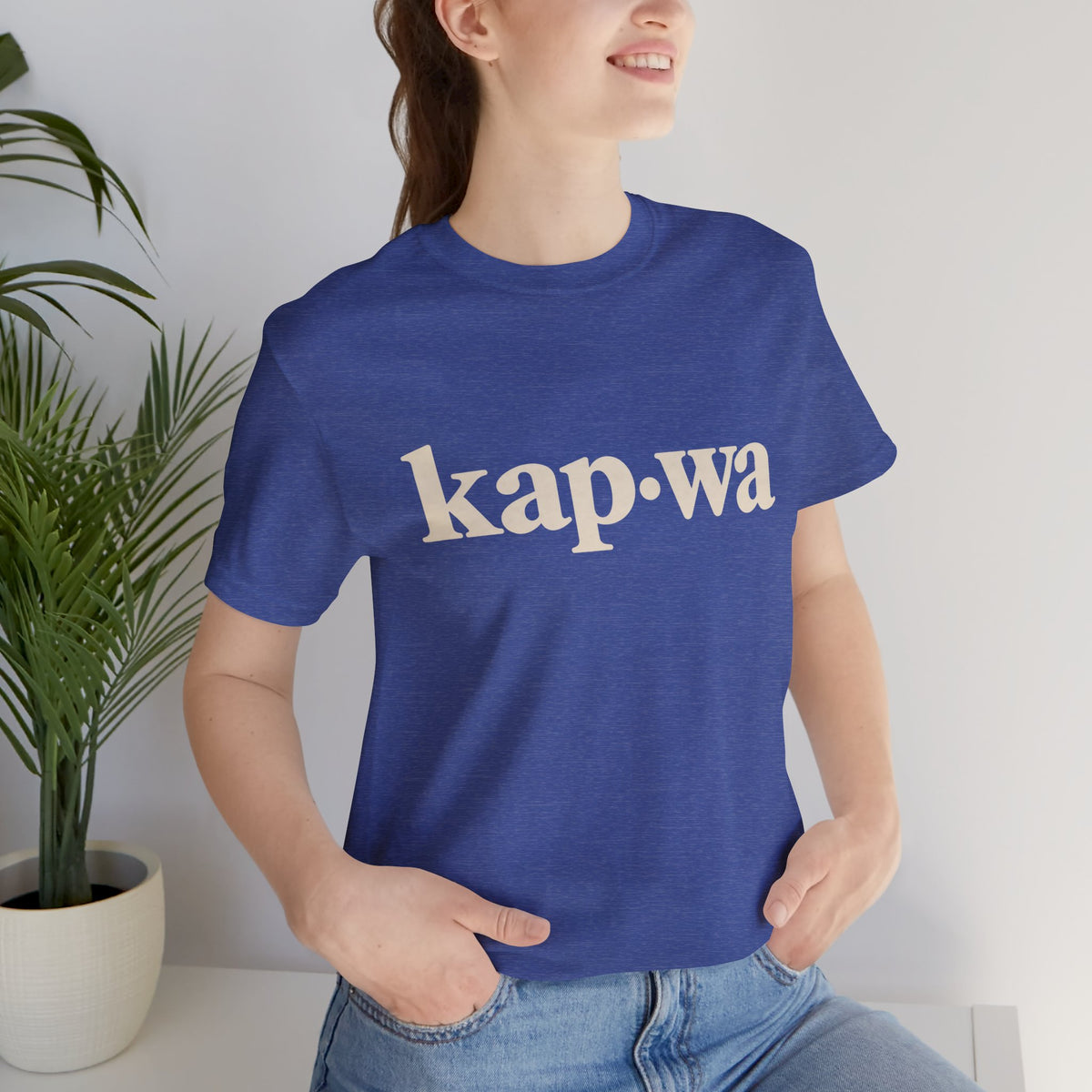 Seated model wearing the Heather True Royal KAPWA Filipino heritage tee, styled casually with the front graphic visible.