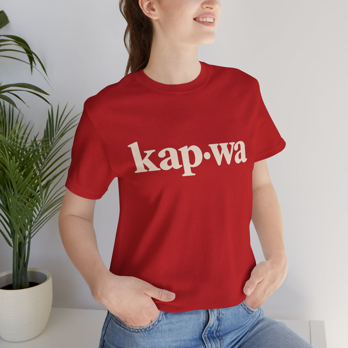 Seated model wearing the Red KAPWA Filipino heritage tee, styled casually with the front graphic visible.