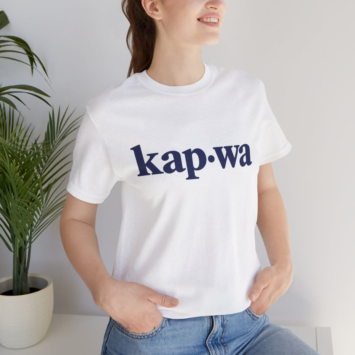 Seated model wearing the White KAPWA Filipino heritage tee, styled casually with the front graphic visible.